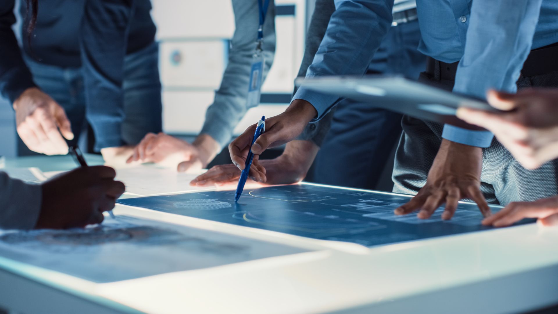 Engineering team reviewing technical drawings on an illuminated design table